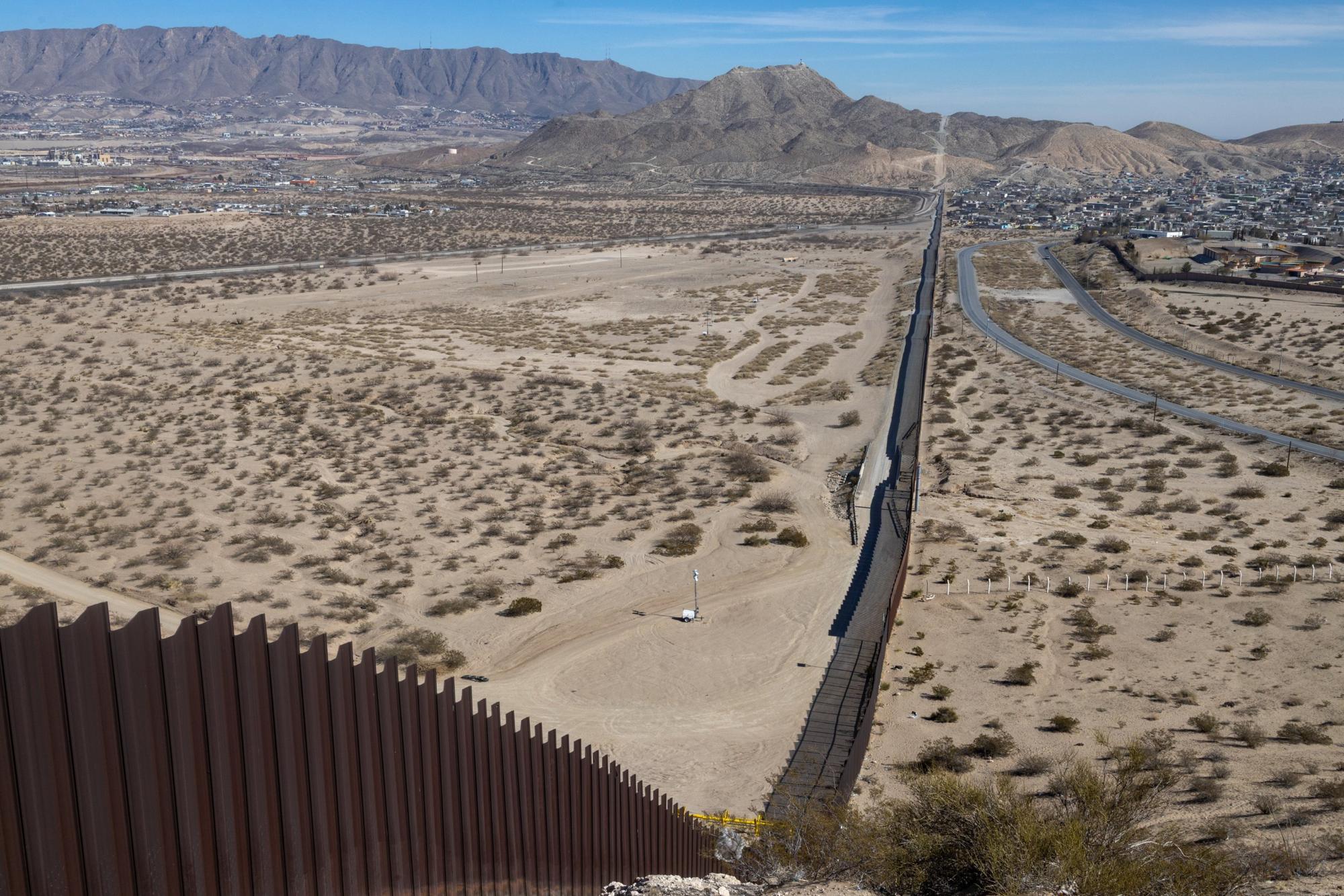 Barrier and patrol road running across open desert toward mountains